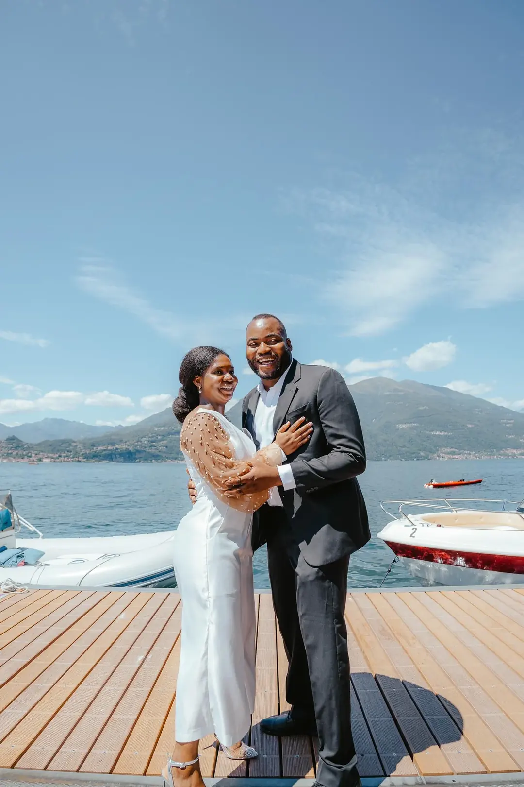 Daniel e Adekunbi ridono su un pontile di legno tra i motoscafi ormeggiati, con le montagne sull'altra sponda alle spalle