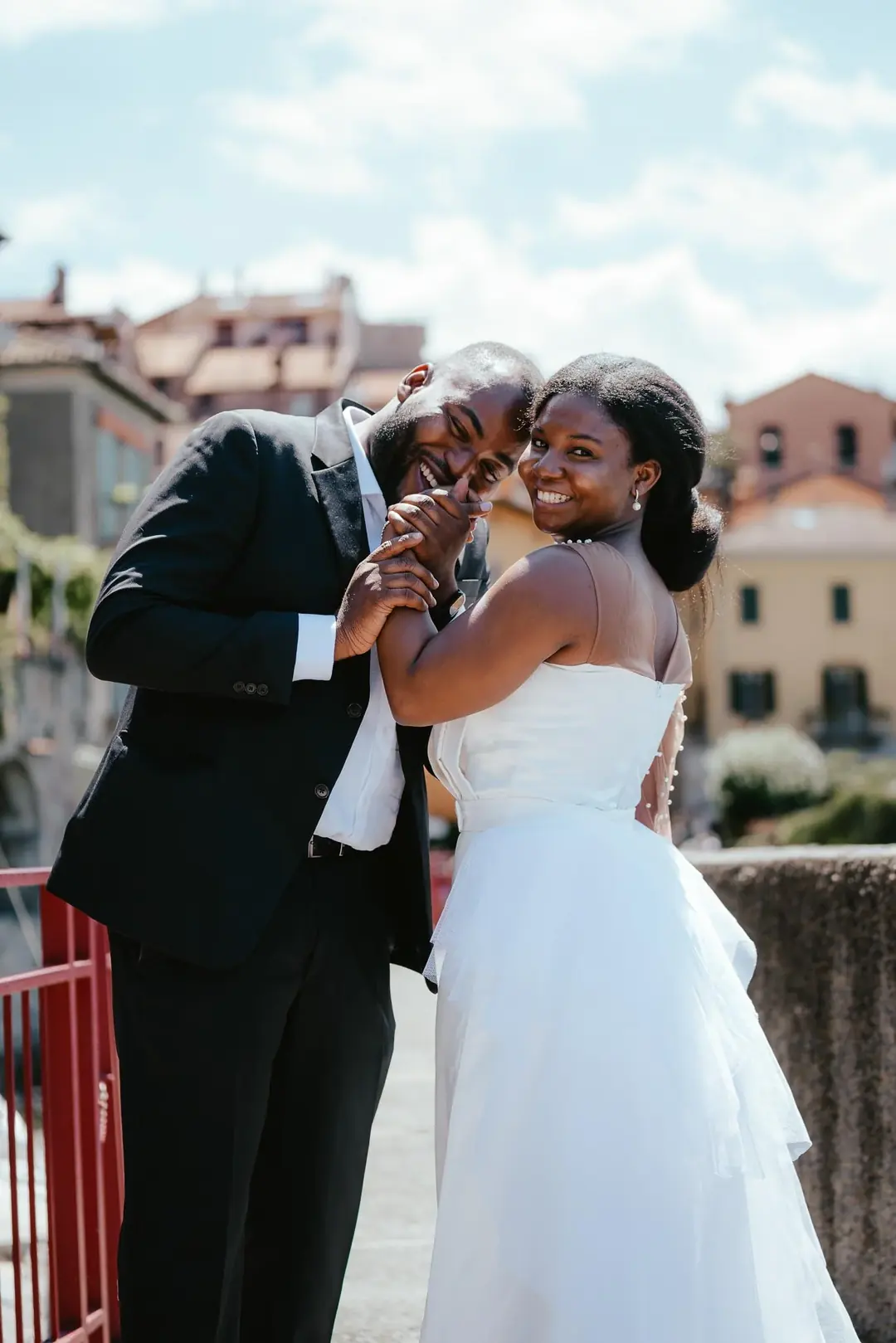 Daniel e Adekunbi ridono insieme, mano nella mano, a una ringhiera rossa con le case alle spalle