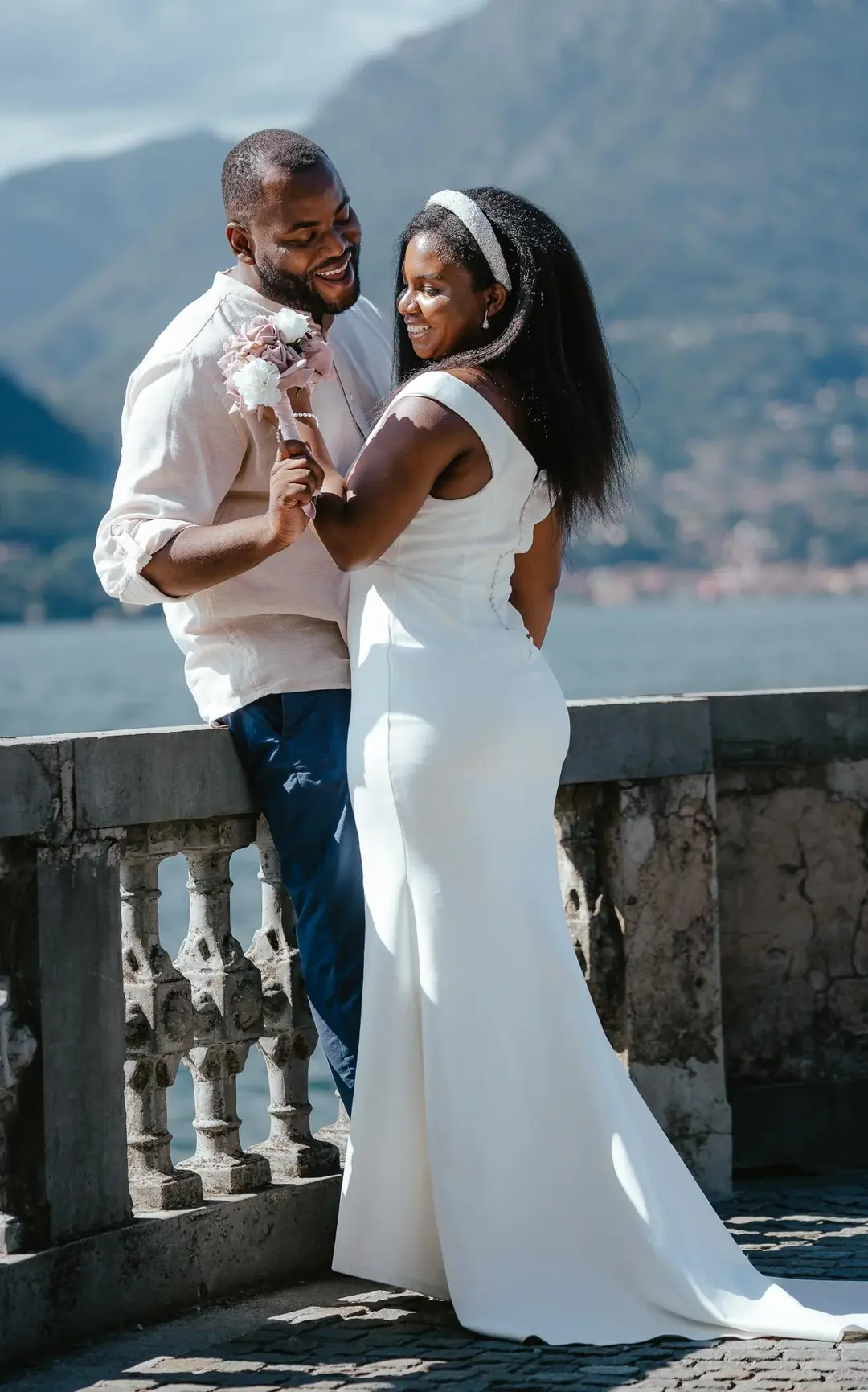 Daniel and Adekunbi laughing against an old stone balustrade, the lake and mountains behind them