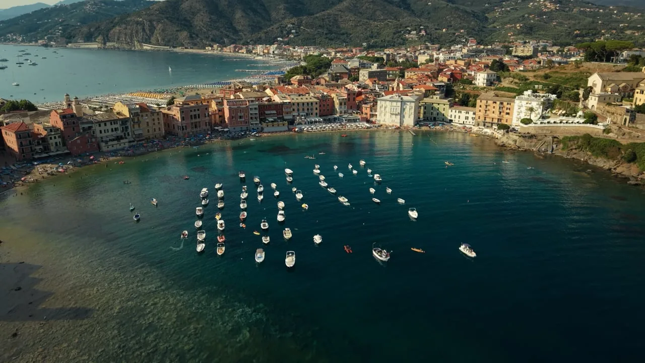 Aerial view of the Baia del Silenzio in Sestri Levante, with small boats moored in a curve of clear water below a line of coloured houses