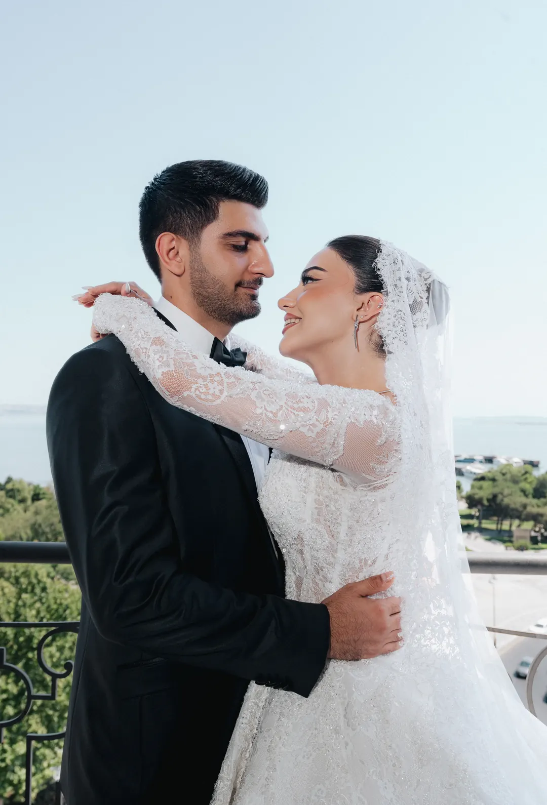 A bride and groom embracing on a balcony high above the sea, her lace veil falling over her shoulder