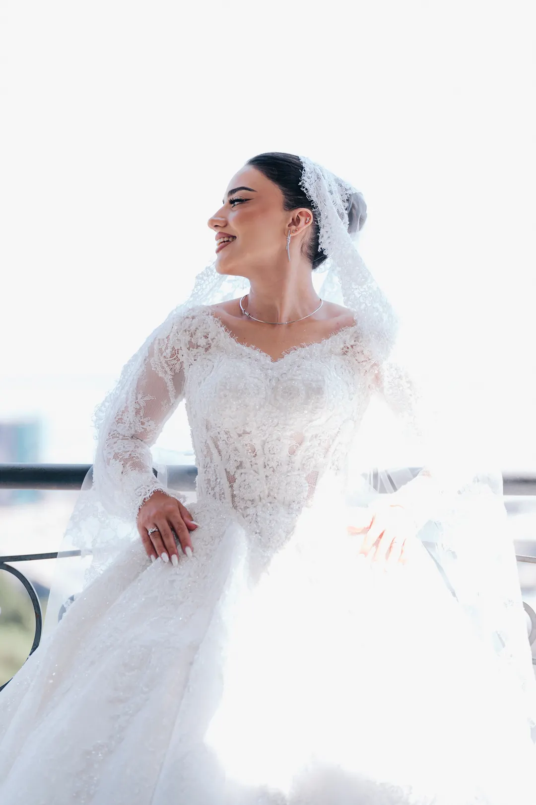 Kimya in her lace wedding gown and veil, smiling in bright daylight on the balcony of her suite in Baku