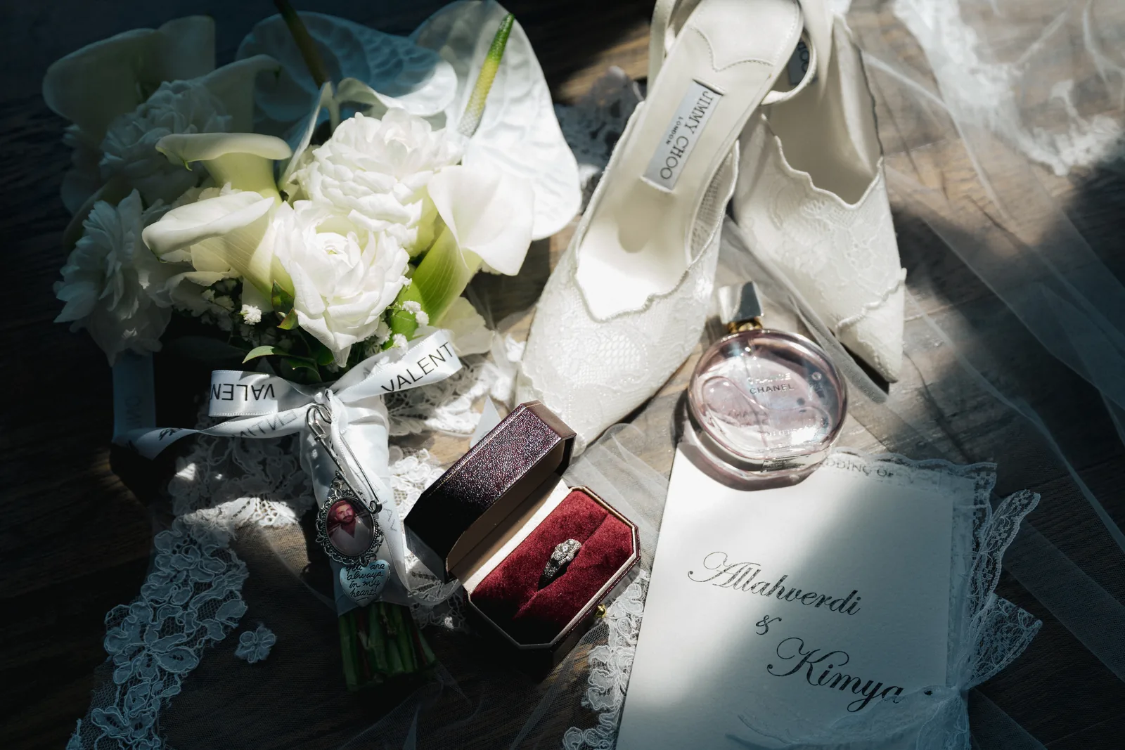 A white bouquet, bridal heels, a ring and a name card laid out in soft window light