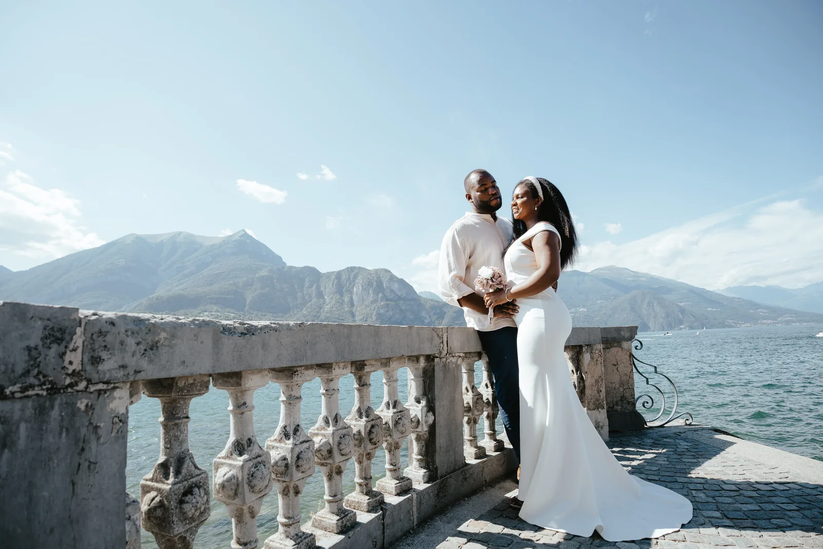 Daniel ve Adekunbi, Bellagio'da arkalarında Alpler olan taş bir korkuluğun yanında