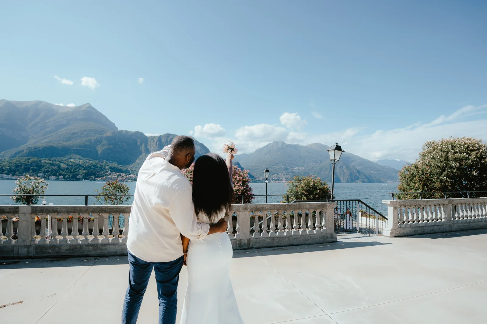 A couple seen from behind on a terrace with a lamppost and mountains across the lake in Bellagio