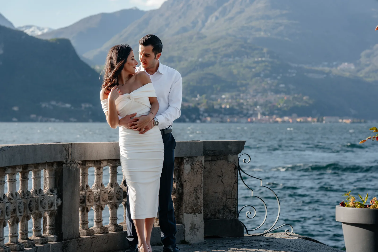 A couple embracing at a balustrade with a village across the lake, elsewhere on Lake Como (not at Villa Monastero)