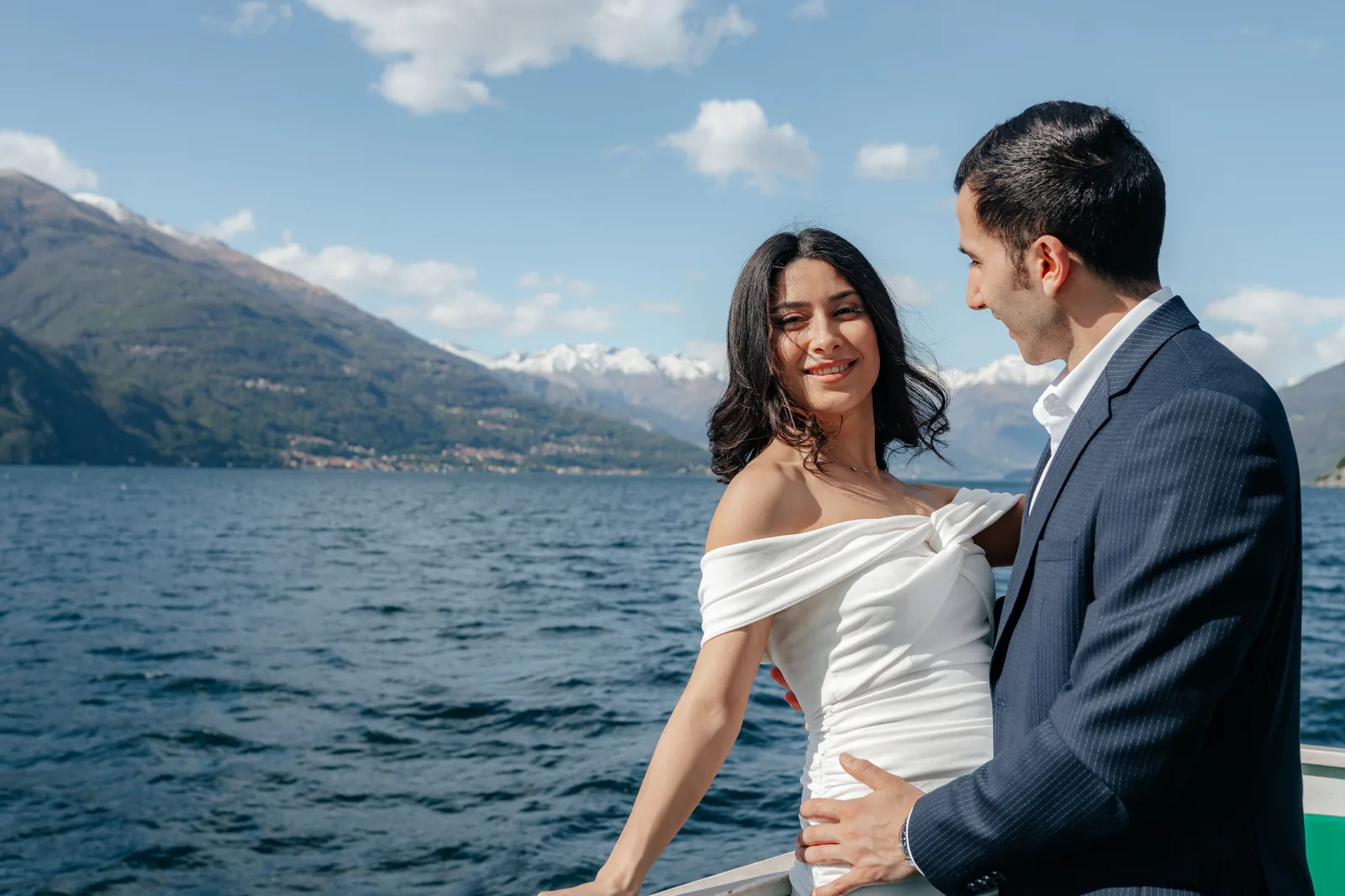 A couple on a boat with snowy peaks behind them, photographed on Lake Como