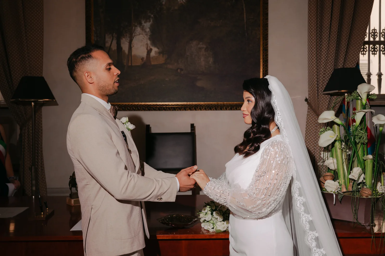 A bride and groom hold hands as they face each other at their civil ceremony at the town hall