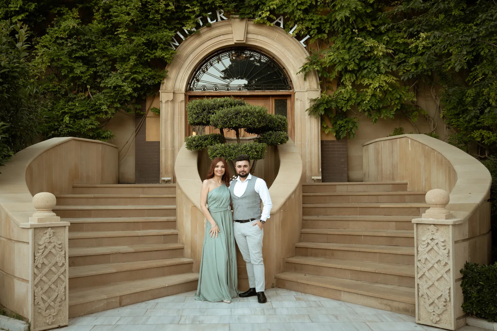 Two guests at the foot of twin curved staircases below an ivy-covered arch (not at Villa Rufolo)