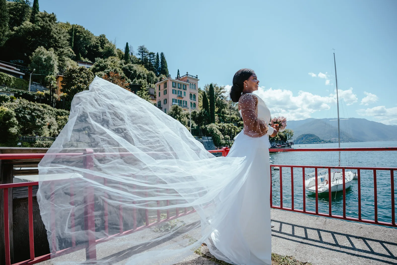 Il velo di una sposa mosso dal vento a una ringhiera rossa sul lago, altrove sul Lago di Como (non a Villa Pizzo)