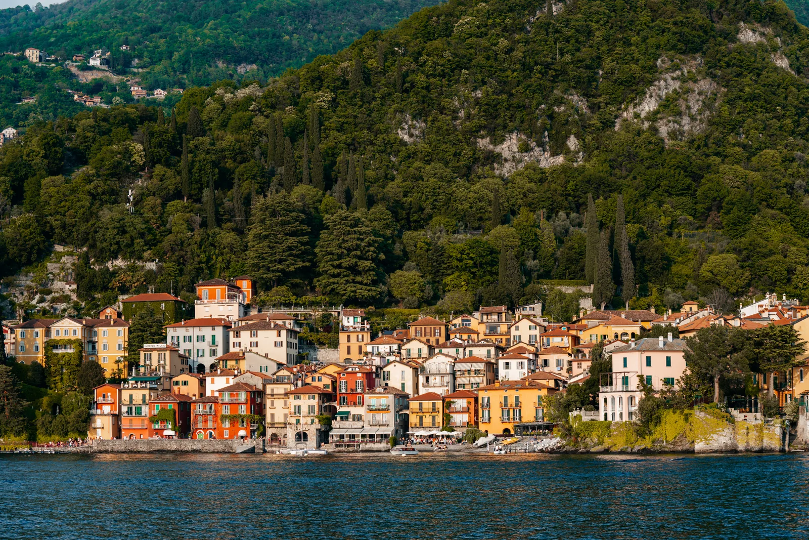 The colourful houses of Varenna on Lake Como seen from the water, below a wooded mountain