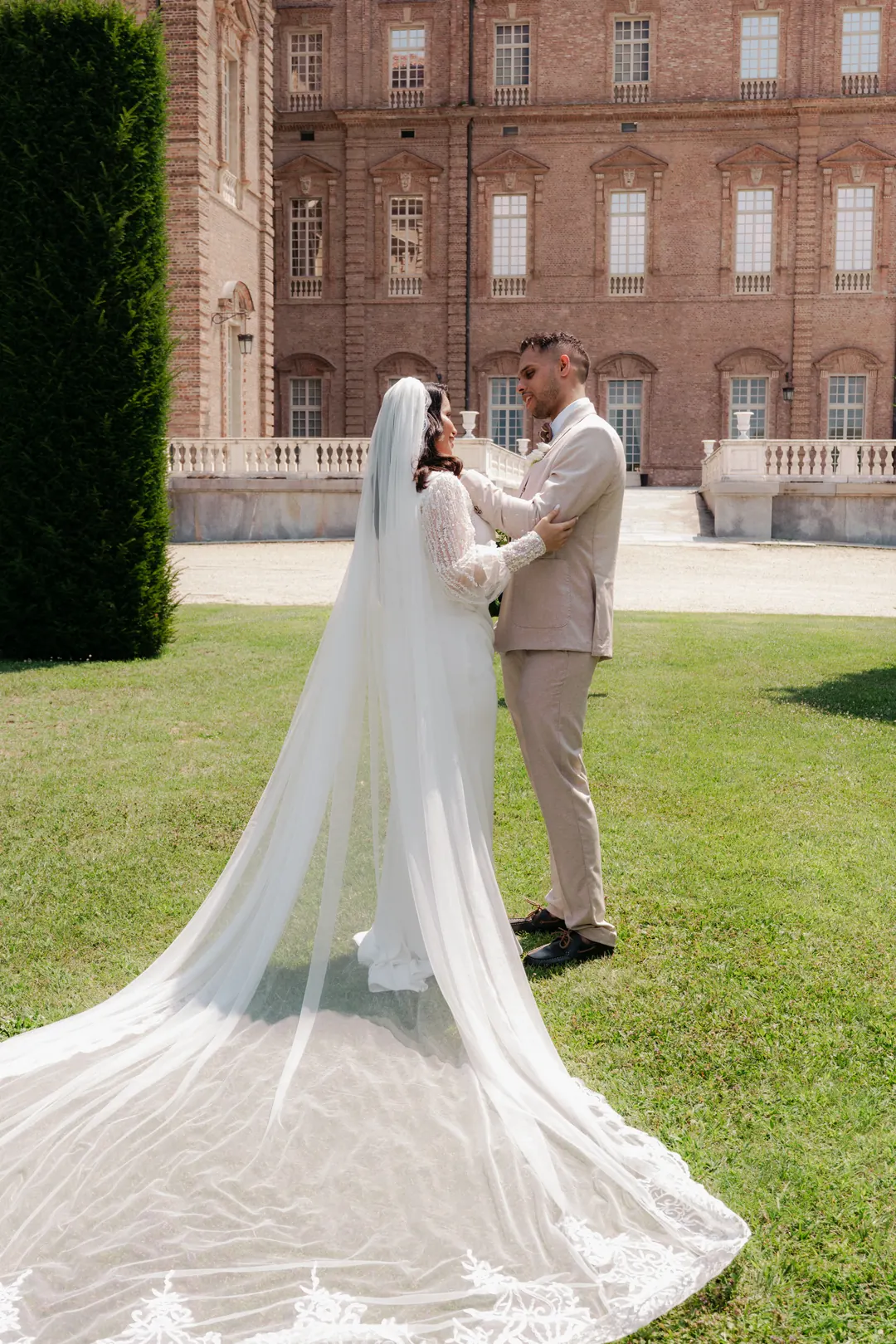 Hejrat's long lace-edged veil spread across the lawn as she holds Mohammed, in front of the brick facade of the Reggia di Venaria