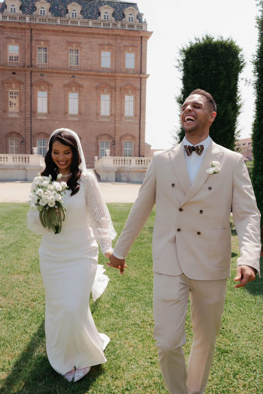 Mohammed laughing as he walks hand in hand with Hejrat across a lawn, the red-brick Reggia di Venaria behind them