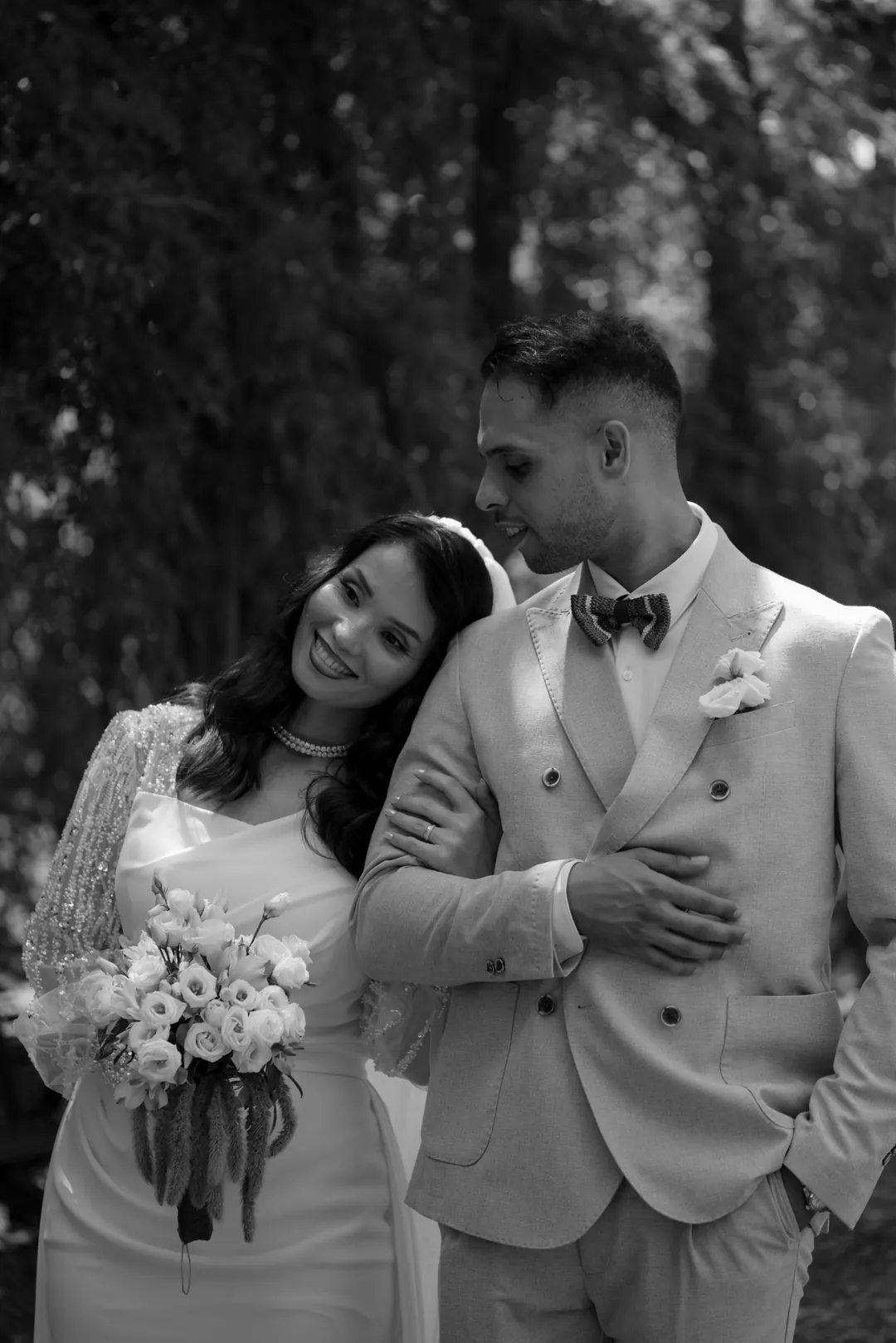 Hejrat leaning her head on Mohammed's shoulder, holding a bouquet of white flowers, in black and white