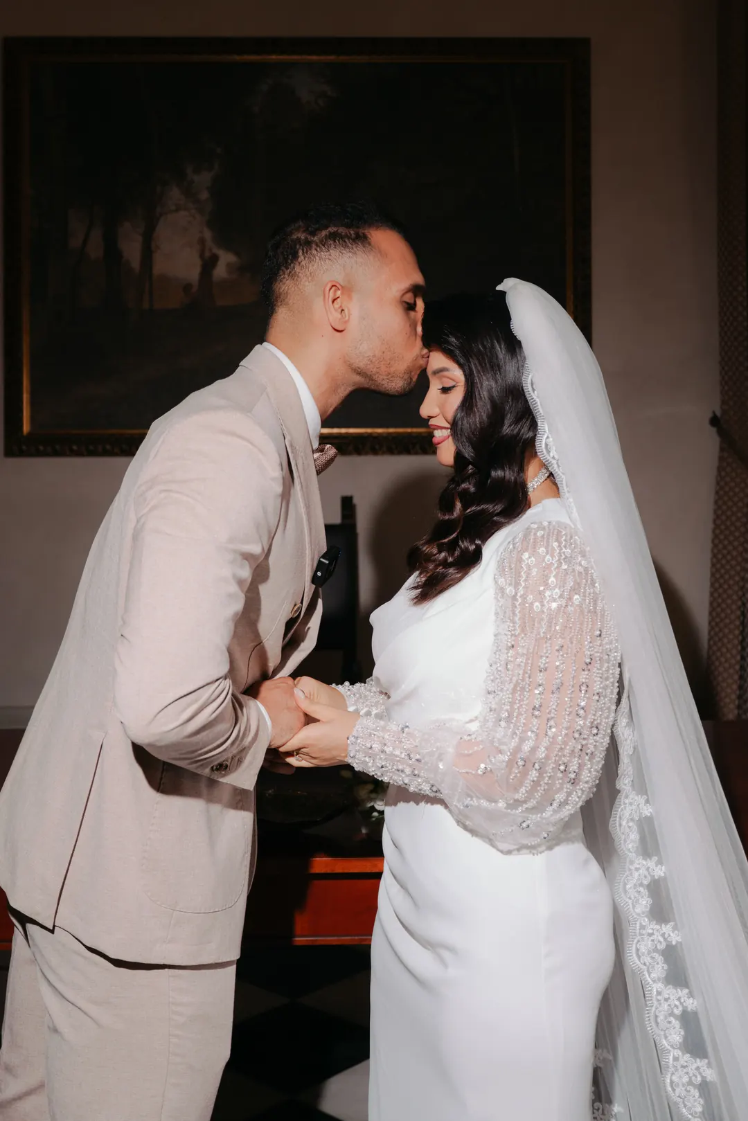 Mohammed kissing Hejrat on the forehead during their civil ceremony, a dark landscape painting on the wall behind